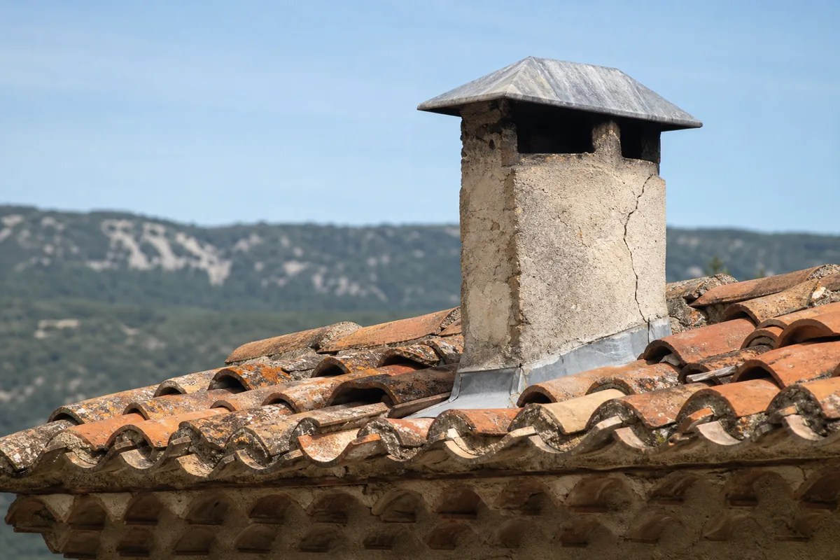 Souche de cheminée en pierre coiffée d’un chapeau de zinc sur une toiture en tuile canal du sud Luberon